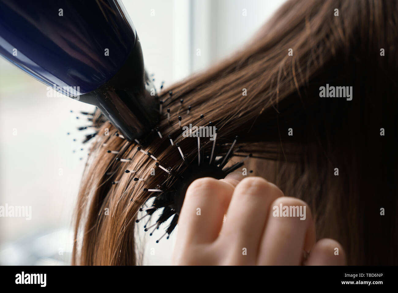 Parrucchiere con asciugacapelli spazzolare i capelli lunghi della giovane donna in salone, primo piano Foto Stock