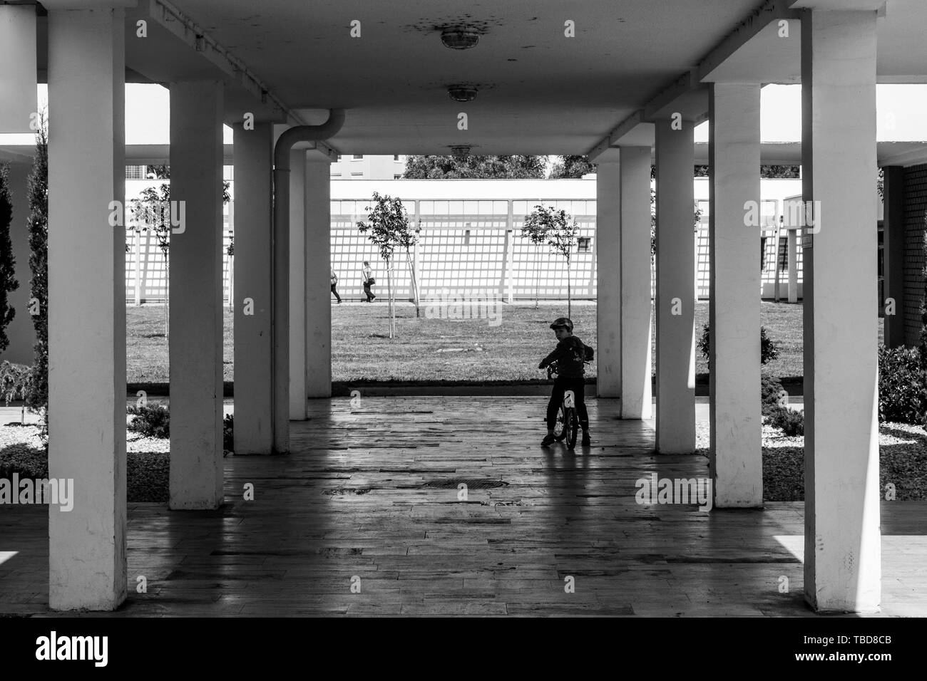 Piazza moderna architettura - colonne di cemento lungo porticato con bambino di equitazione Foto Stock