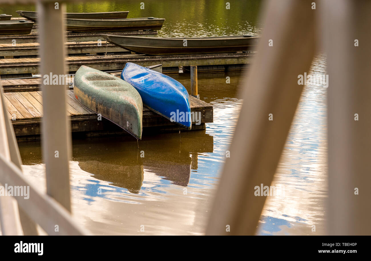 Canoe colorate memorizzati capovolto su un dock su un lago con le nubi riflessi nell'acqua Foto Stock