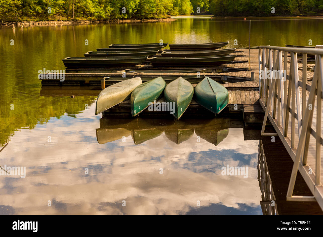 Green canoe memorizzati capovolto su un dock su un lago con le nubi riflessi nell'acqua Foto Stock