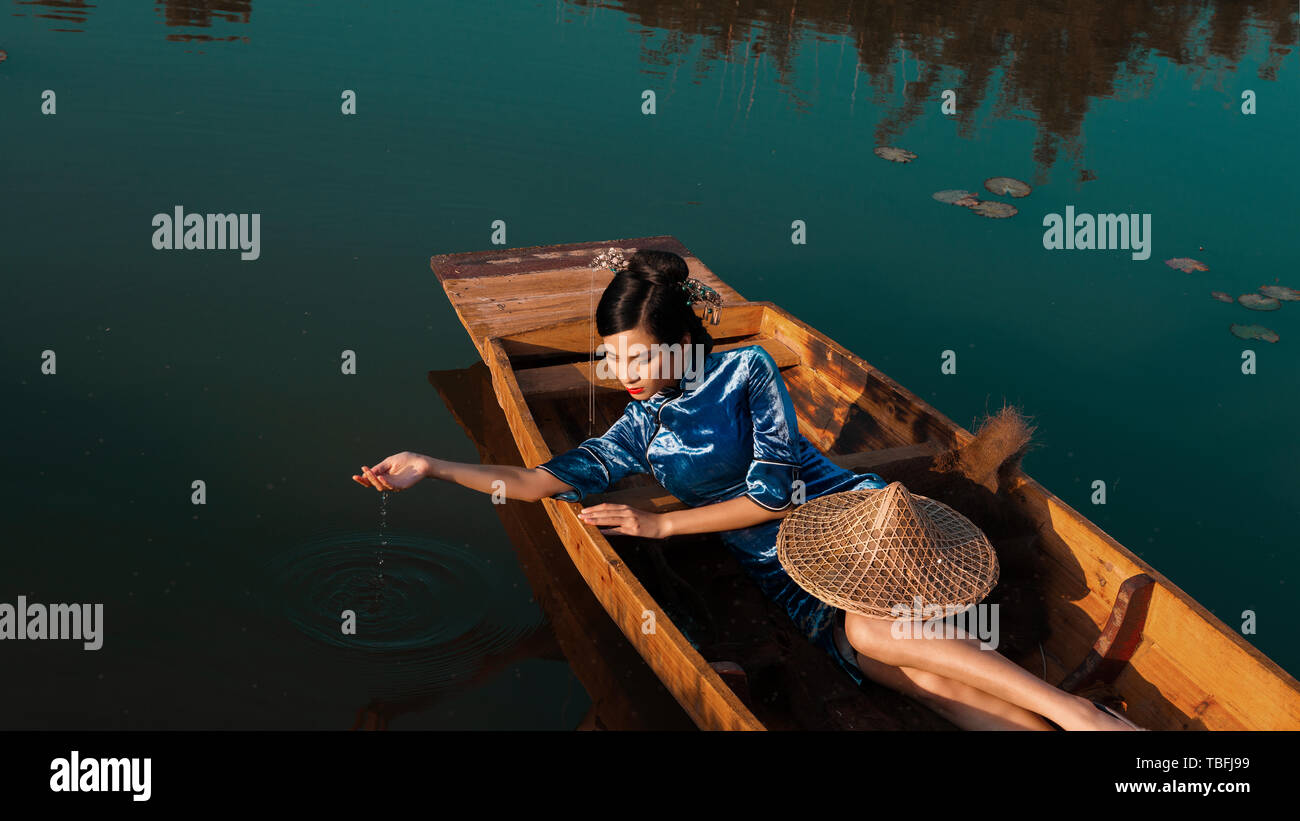 La ragazza è situata su di una piccola imbarcazione in legno sulla superficie del lago, raccogliendo le acque del lago con le sue mani, il gocciolamento di acqua dalle sue dita, il cappello Foto Stock