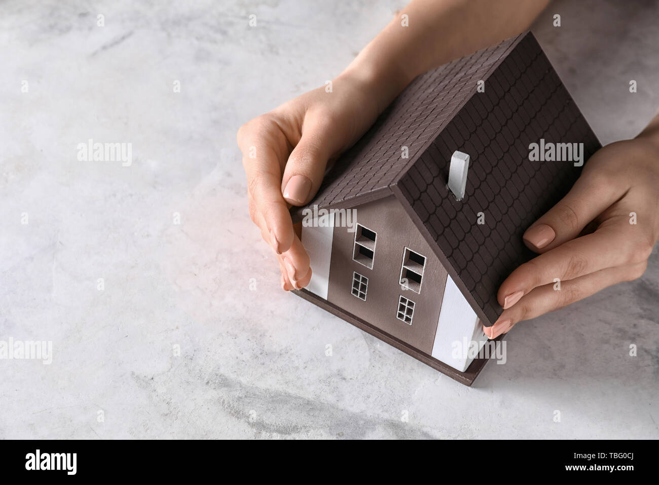 Mani femminili con il modello di casa su sfondo grigio. Concetto di terremoto Foto Stock