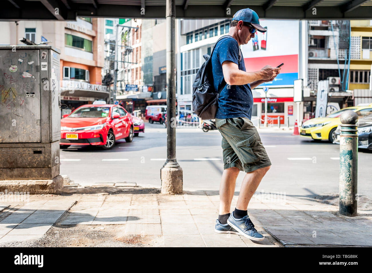 Un turista occidentale controlla il suo telefono come fa il suo modo lungo Sukhumvit Road, Bangkok, Thailandia, Sud Est Asiatico. Foto Stock