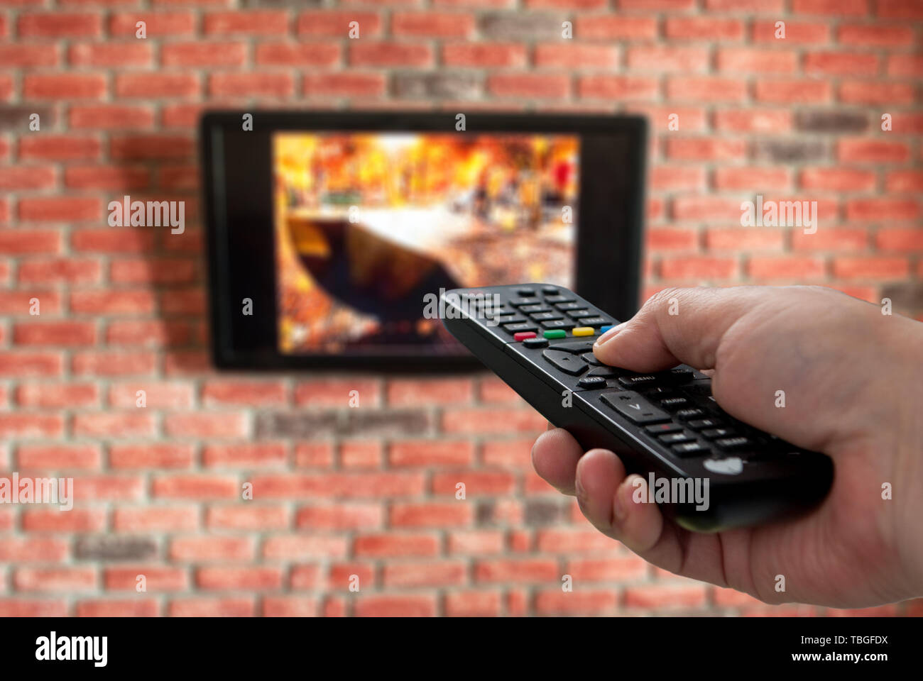 TV con telecomando in mano e un muro di mattoni in background per lo sfondo Foto Stock