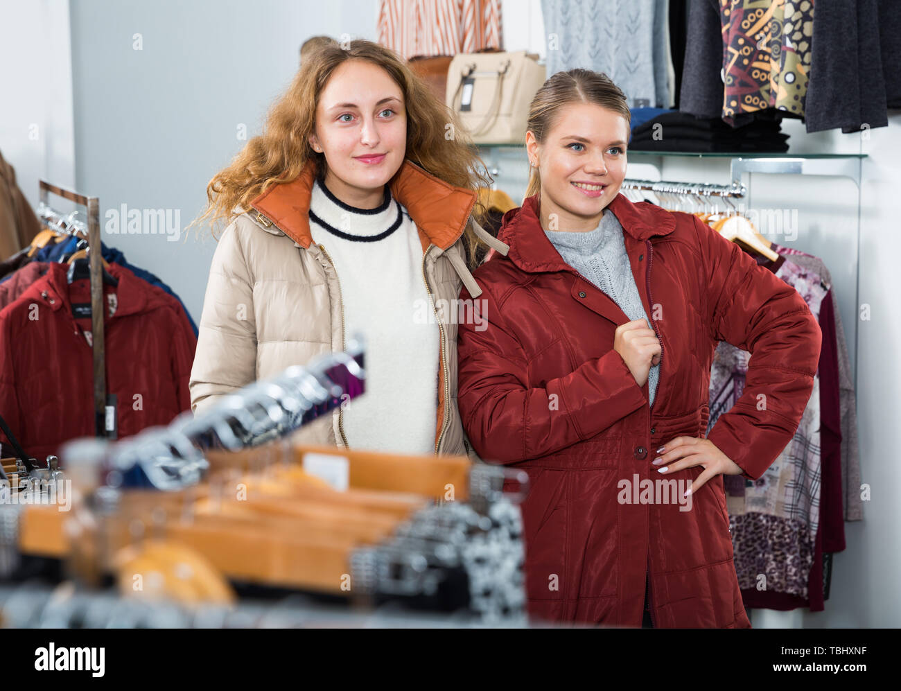Due giovani donne positive in posa di cappotti in cappotti boutique di abbigliamento Foto Stock