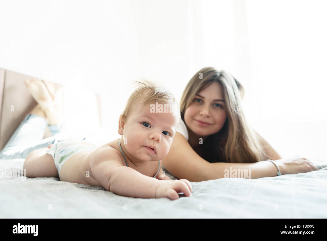 La madre con il figlio neonato sdraiato sul letto in i raggi di luce solare Foto Stock