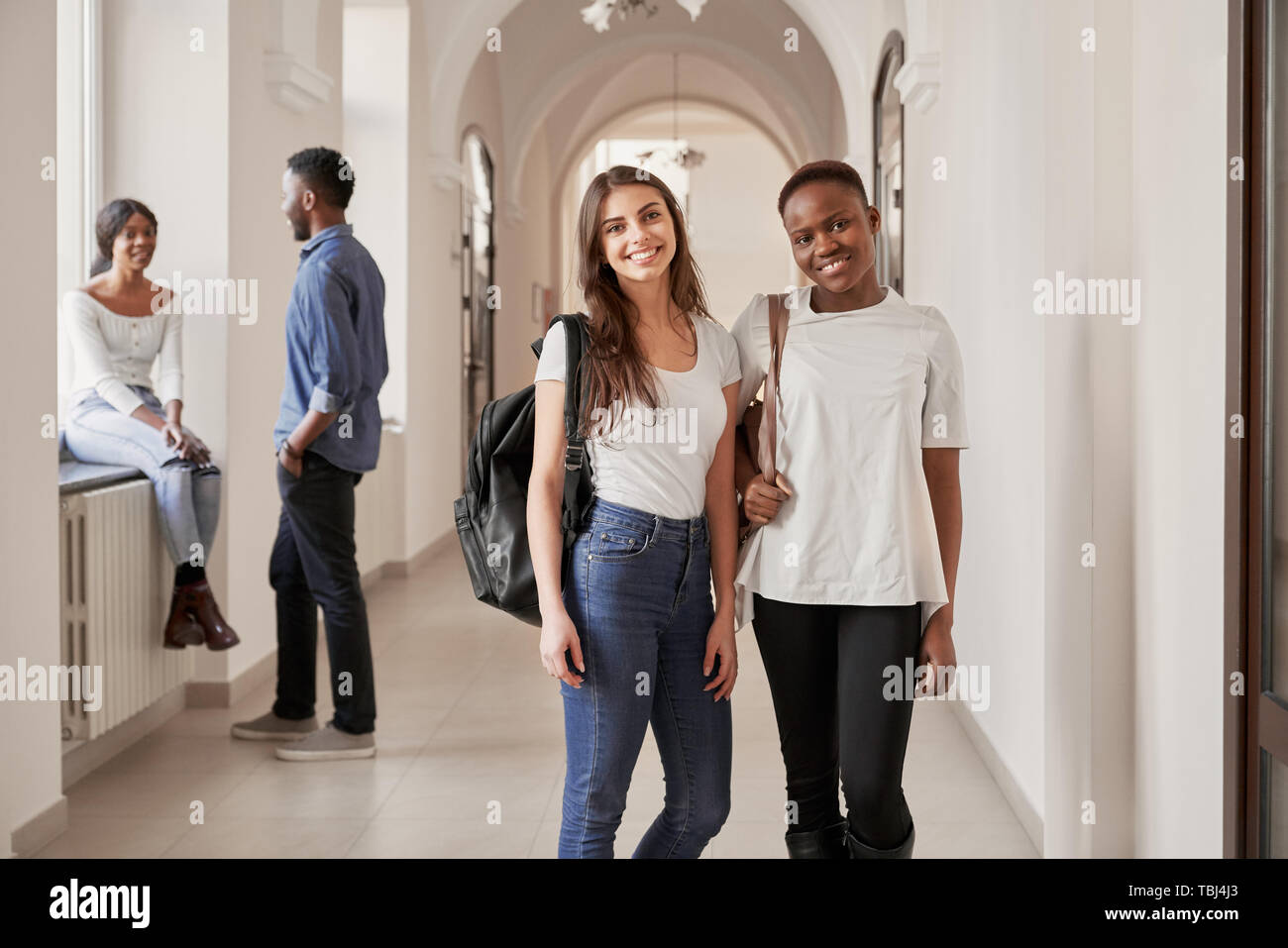 Vista frontale della Peste e Caucasico studentesse in appoggio sul corridoio e sorridente alla fotocamera. Le belle donne mantenendo gli amici, studiare in università internazionale. Concetto di amicizia internazionale. Foto Stock