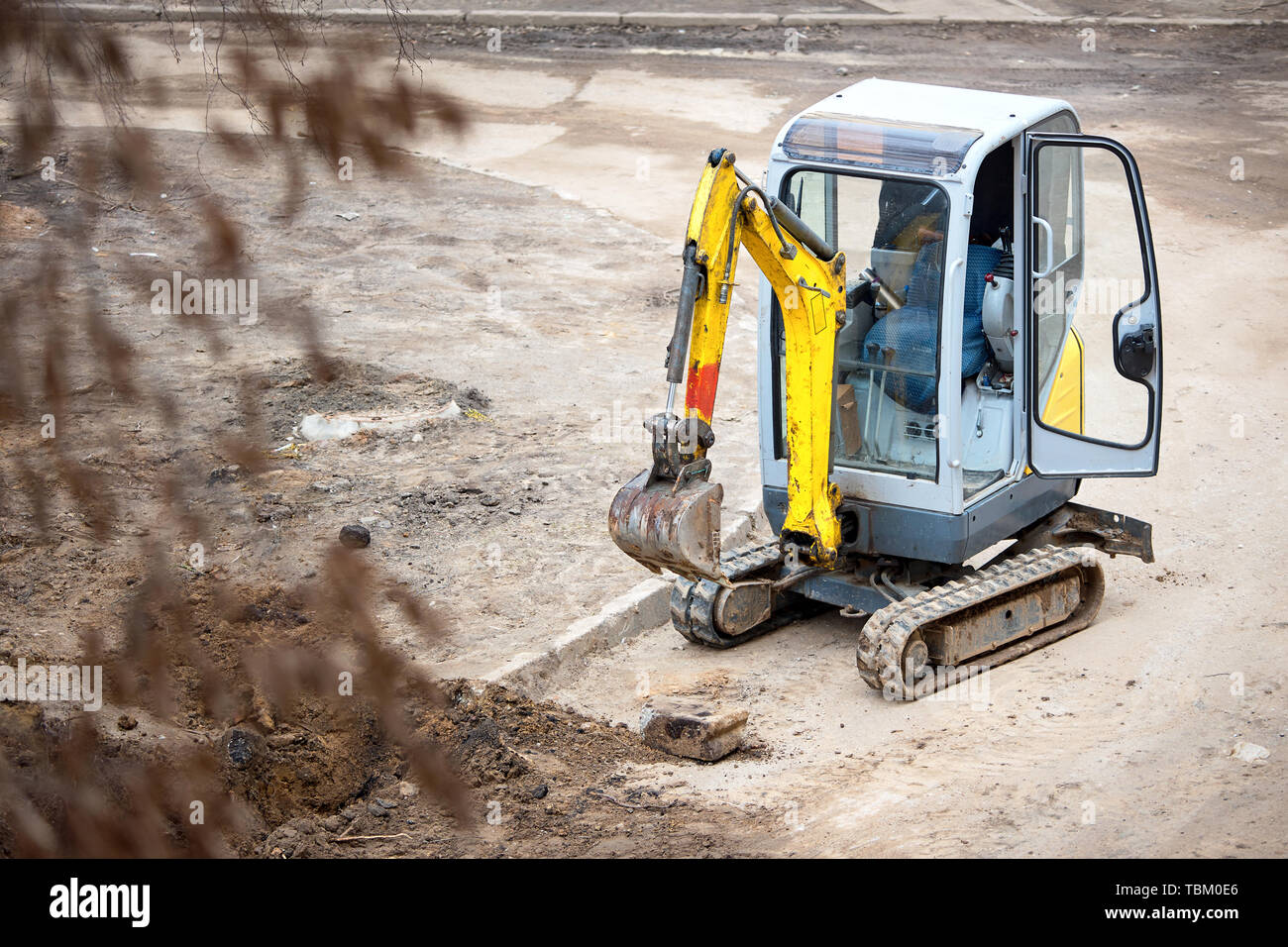 Tracked mini escavatore scoppia cordoli vecchia prima di installare nuovi cordoli. Il concetto di uso economico ed attrezzatura compatta per le esigenze urbane. Foto Stock