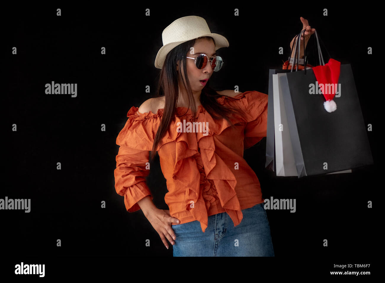 Asian shopping donna sorpreso con il Venerdì nero shopping bag e Santa Claus hat interno su sfondo nero. Gli appassionati di shopping e bellezza tema di moda. Foto Stock