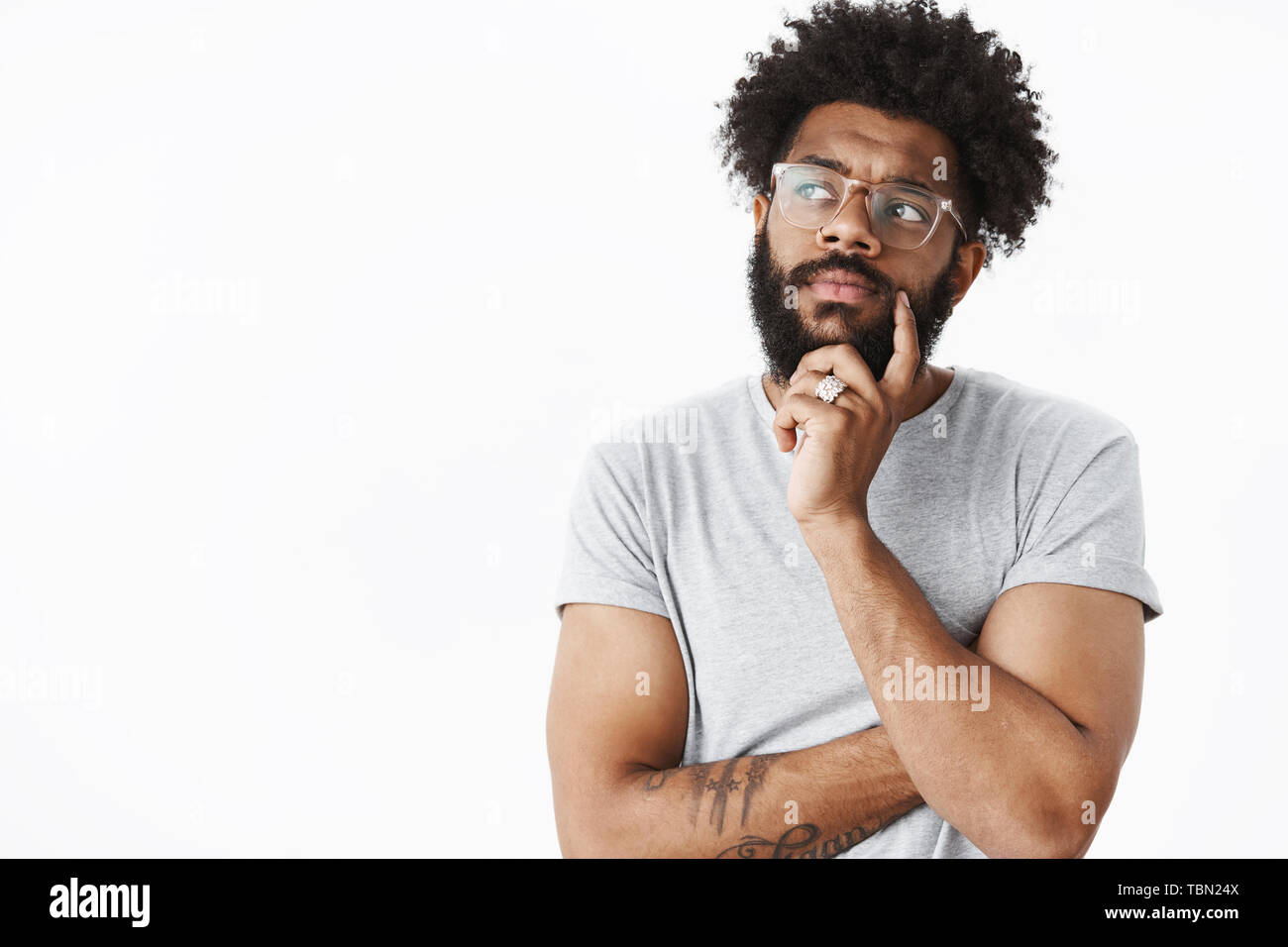 African American guy in bicchieri rendendo piano in mente pensando a lista della spesa tenendo la mano sulla barba guardando a sinistra riflessivo, accigliata come considerando wh Foto Stock