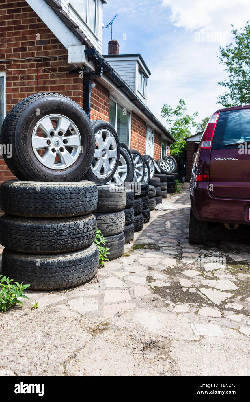 Una fila di ruote e pneumatici impilati in imposta al di fuori di un edificio in un auto scrapyard interruttori Foto Stock