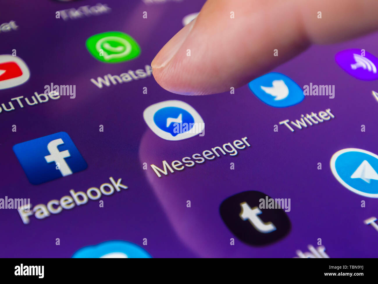 Dito che preme un'icona su uno smartphone o un tablet PC touchscreen per caricare il Facebook Messenger social media messaging app. Foto Stock