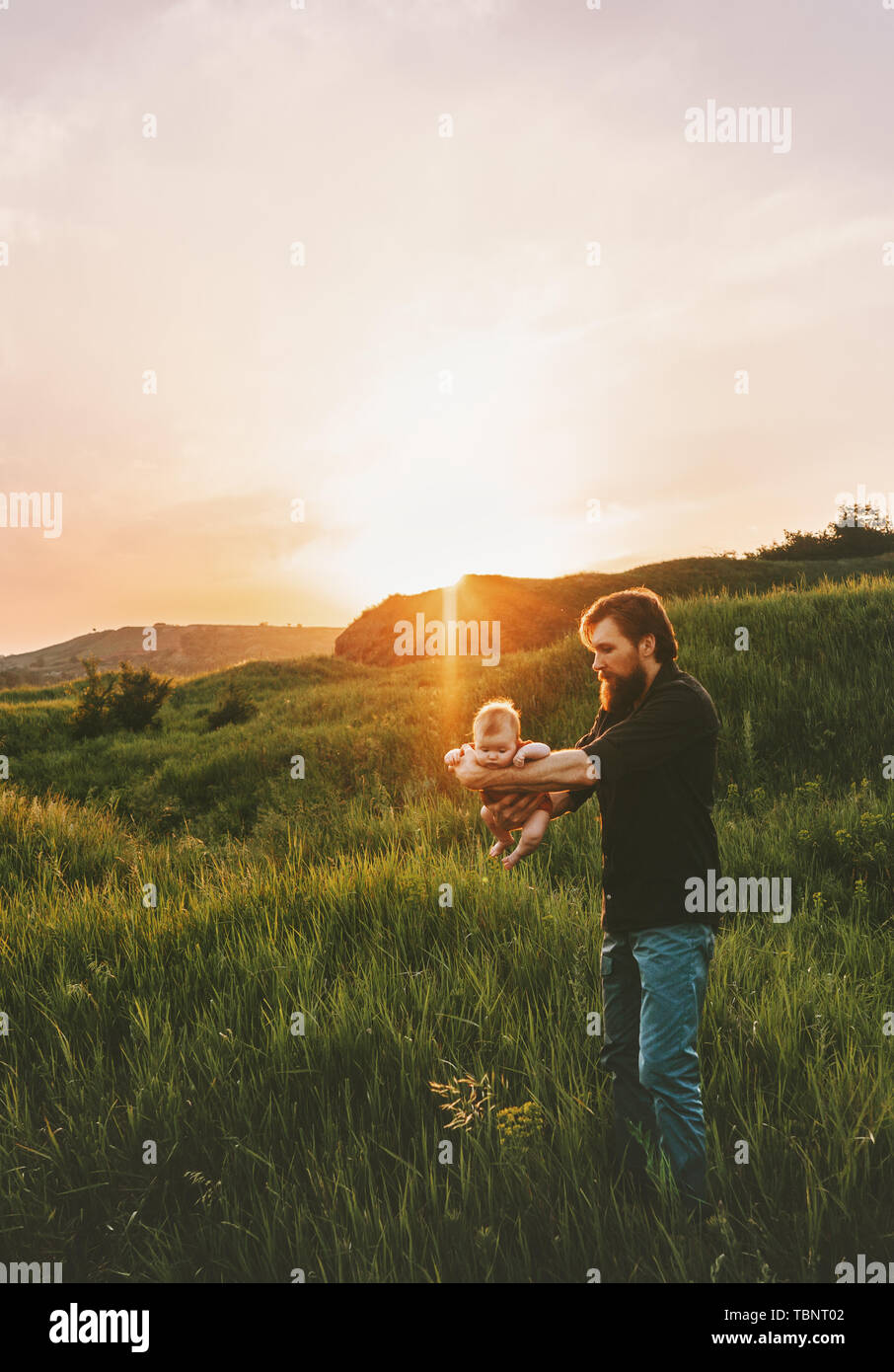 Padre tenendo il bambino al di sopra di erba a camminare in montagna famiglia outdoor lifestyle papà e bambino viaggi vacanze estive padri giorno panorama al tramonto Foto Stock