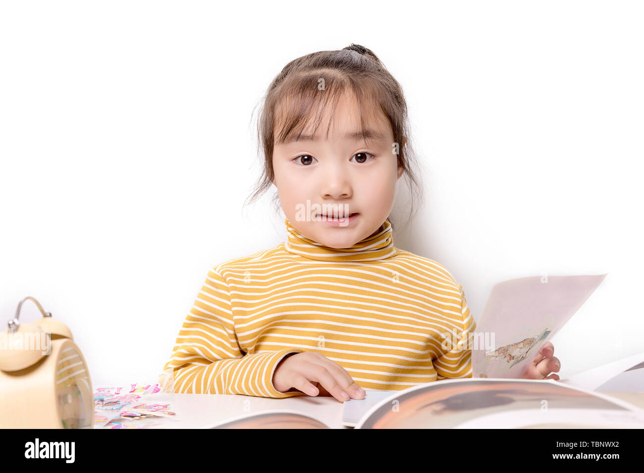 Carino asian bambina la lettura di un libro di fronte a uno sfondo bianco Foto Stock