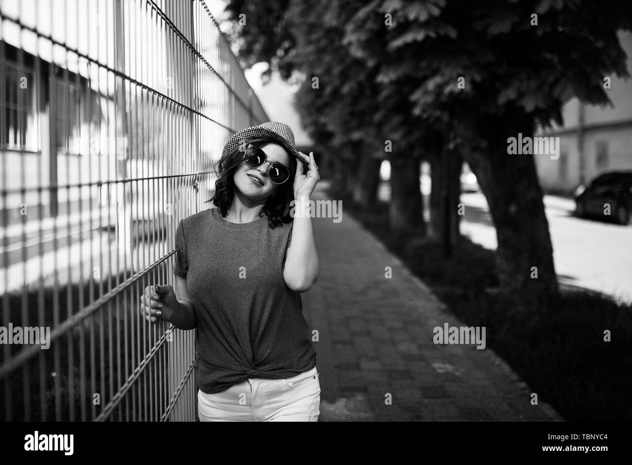 Giovane bella bruna passeggiando per la città in una giornata di sole, vestito in abiti estivi e il cappello sulla sua testa. Foto Stock