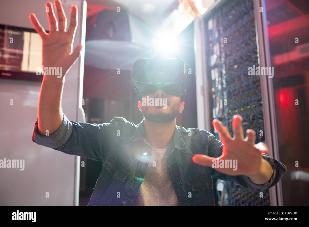 Grave moderno specialista IT con la barba a lavorare nel centro dati e il monitoraggio dei sistemi server mentre utilizzando la realtà virtuale occhiali, effetto luce solare Foto Stock