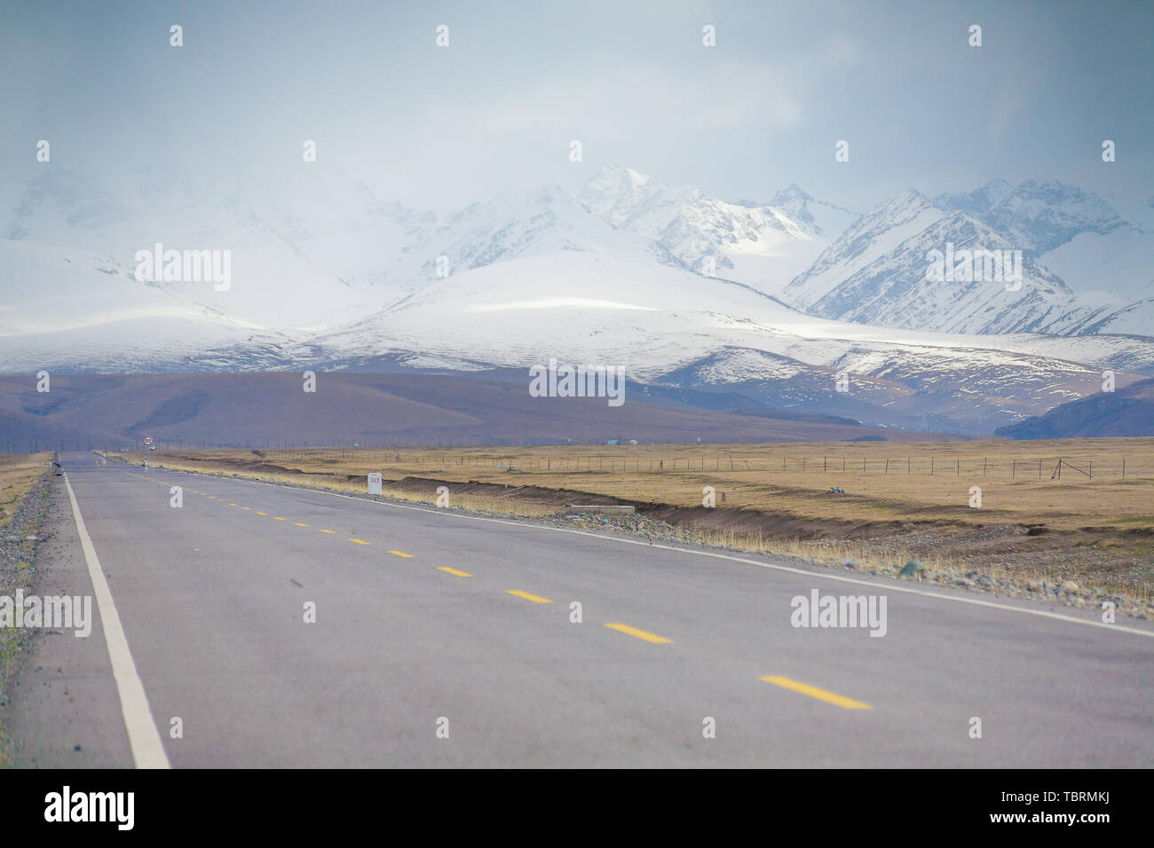 In primavera, la strada della prateria Bayinbru sezione dell'autostrada Doku è accompagnato da alti, continuo montagne innevate. Foto Stock