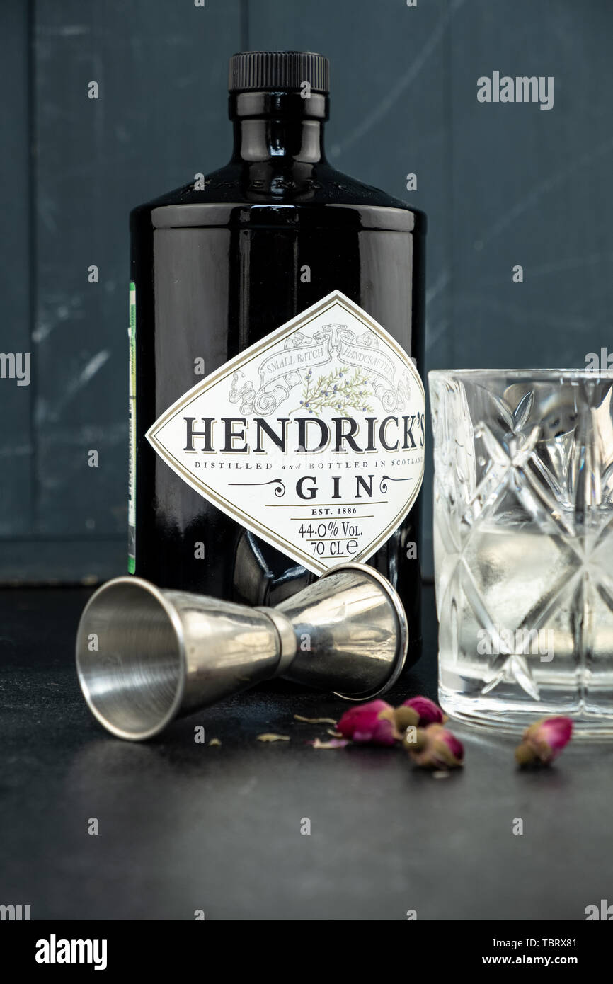 70 cl bottiglia Hendricks gin distillato con vetro e ghiaccio sul rustico scuro dello sfondo. I laici accanto allo Shaker e malenikie le rose rosa. Foto Stock