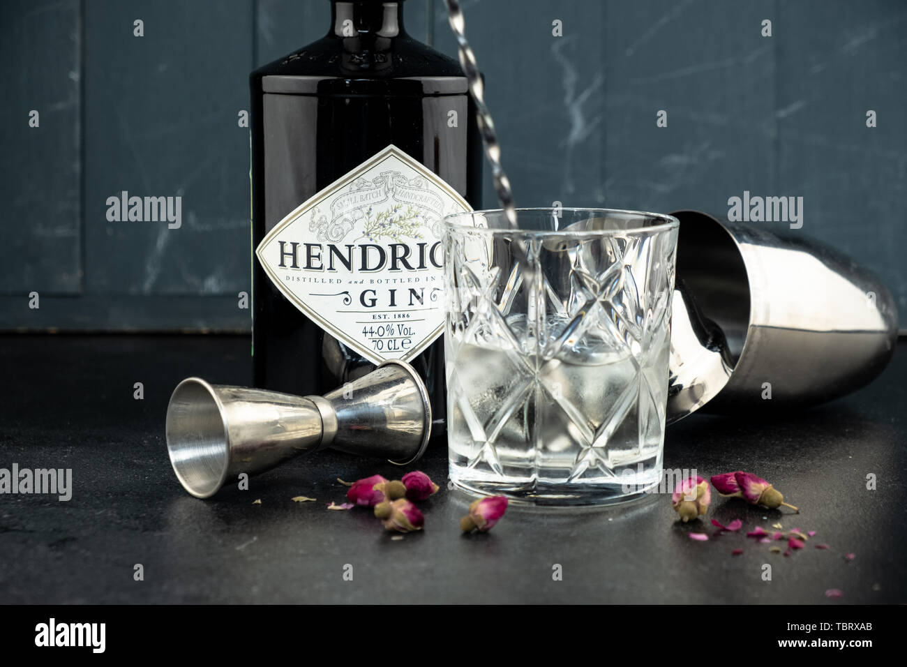 70 cl bottiglia Hendricks gin distillato con vetro e ghiaccio sul rustico scuro dello sfondo. I laici accanto allo Shaker e malenikie le rose rosa. Foto Stock