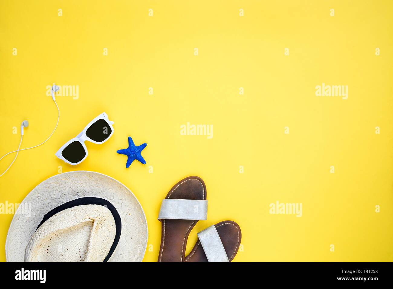 La vacanza estiva accessori. Cappello di paglia, bianco occhiali da sole, auricolari e flip-flop su sfondo giallo. Spazio di copia, piatto laici. Foto Stock