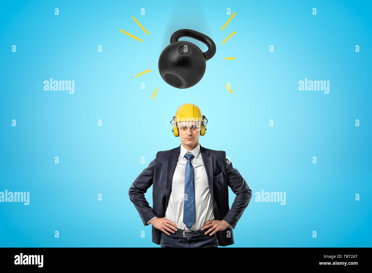 Ritaglia immagine di imprenditore in giallo Casco con paraorecchie, in piedi con le mani sui fianchi e grande kettlebell pesante cadere sulla sua testa. Foto Stock