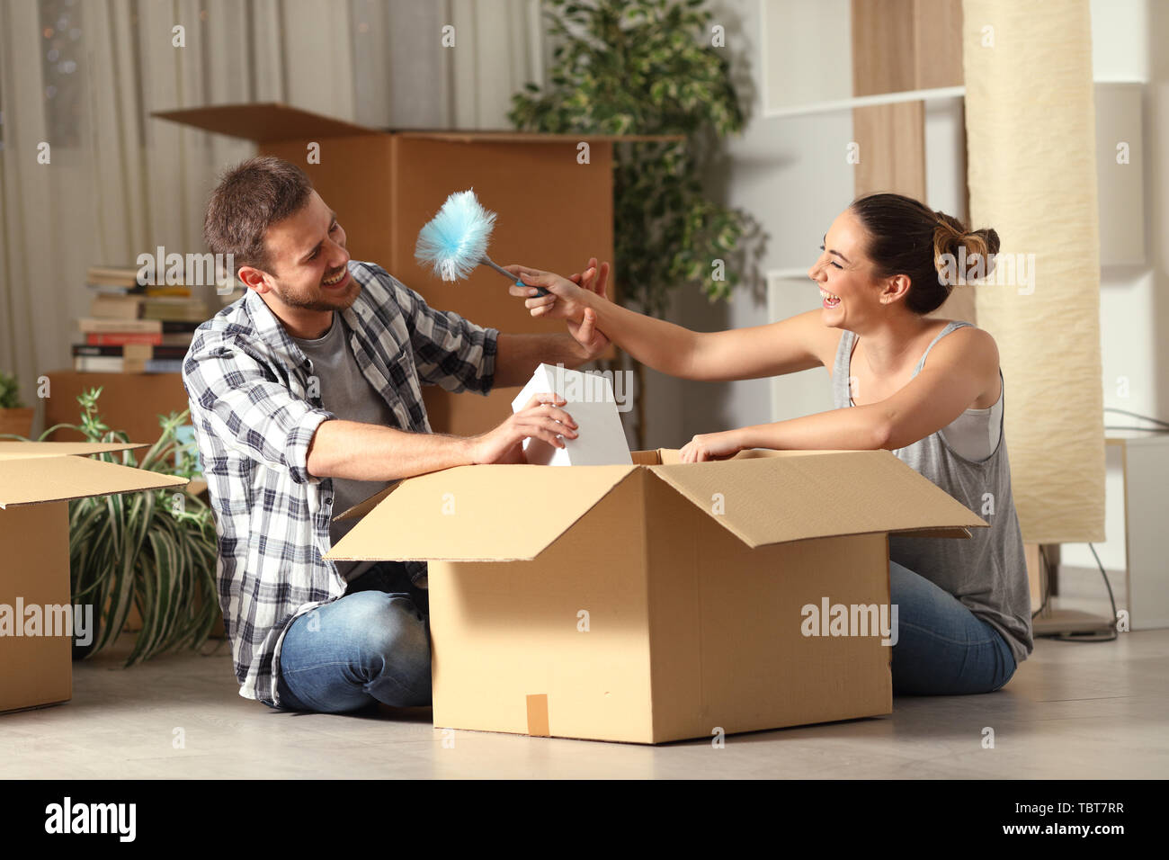 Coppia felice scherzando con un duster pulire unboxing di oggetti in movimento home Foto Stock