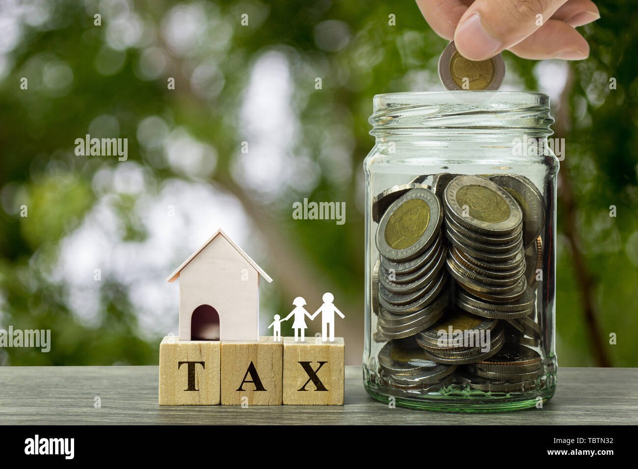 Di proprietà o di tassa immobiliare di concetto. Mano azienda coin sulla pila di monete in un vaso e piccola casa residenziale modello con la famiglia sul blocco di legno su legno Foto Stock