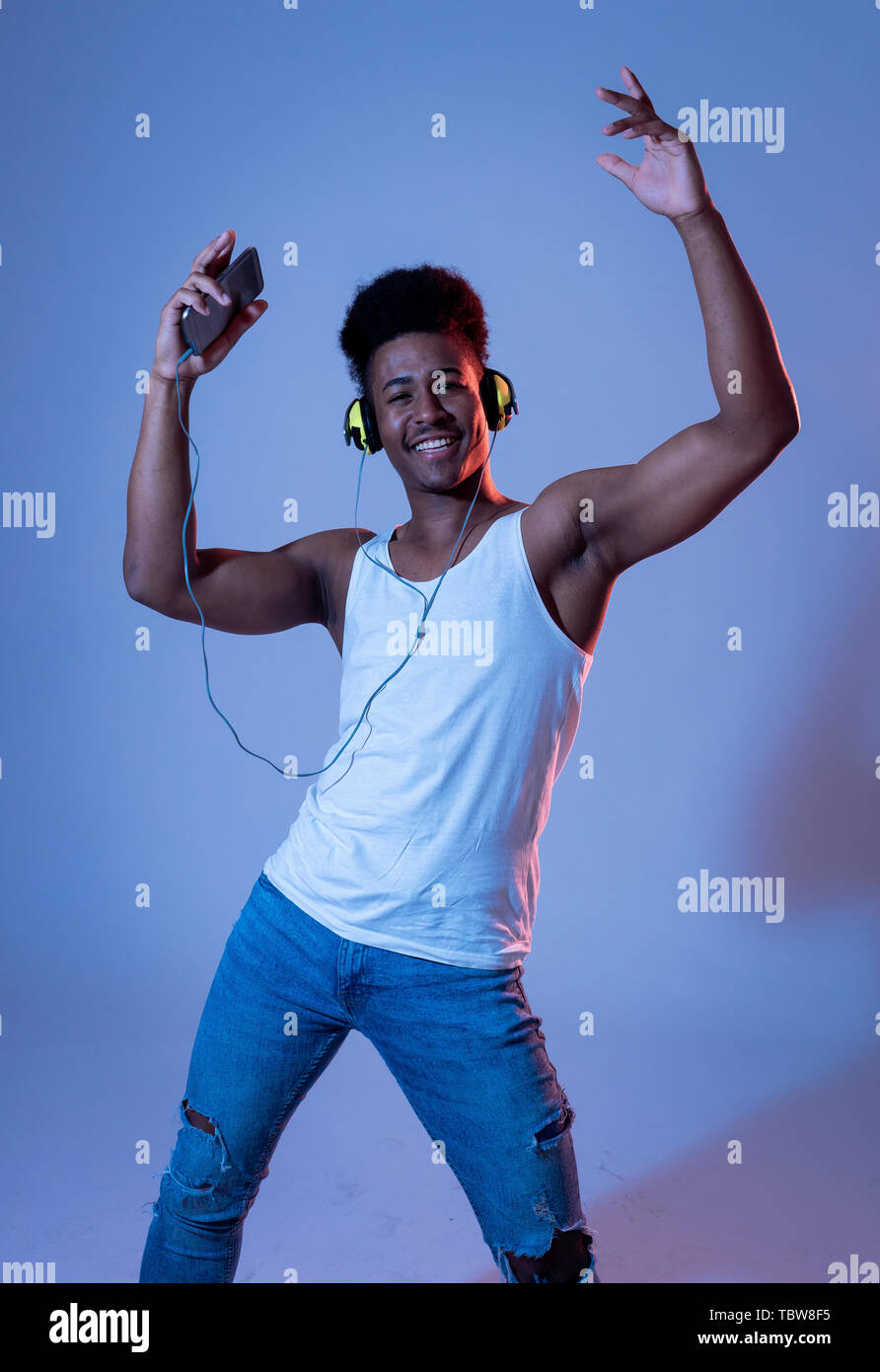 Forte americano africano giovane ballerino uomo ascoltare musica online ballare e cantare con le cuffie. Ritratto artistico con pista da ballo neon Foto Stock