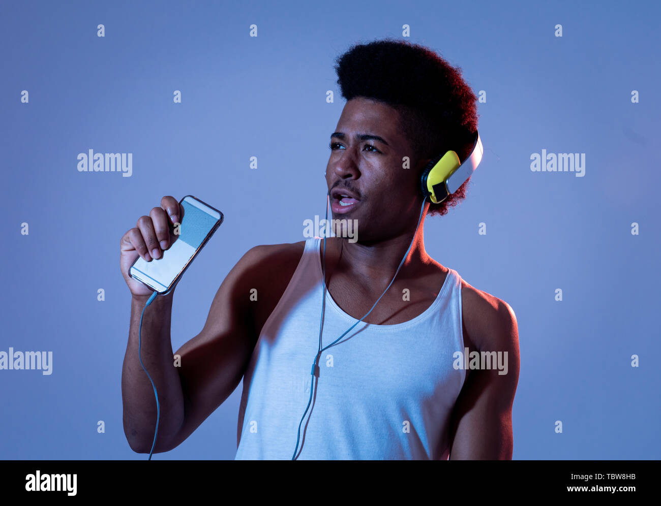 Forte americano africano giovane uomo ascoltare musica online in app per smartphone per ballare e cantare con le cuffie. Close up ritratto con discoteca dance Foto Stock