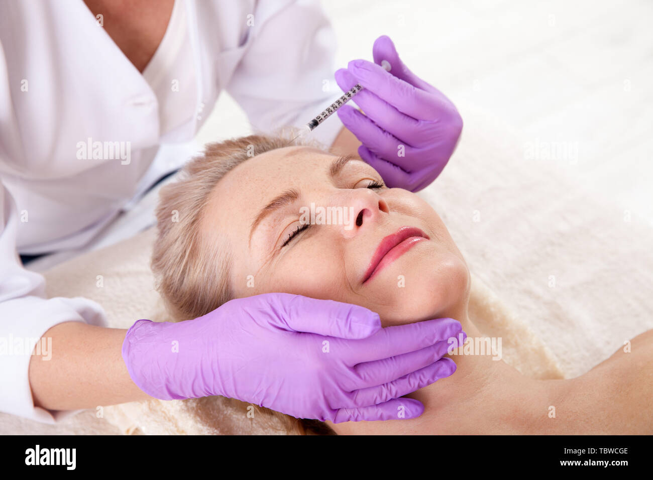 Donna di mezza età riceve iniezione cosmetici nella sua fronte. Iniezione di acido ialuronico per il ringiovanimento del viso procedura. Le donne in un salone di bellezza. Plastica Foto Stock