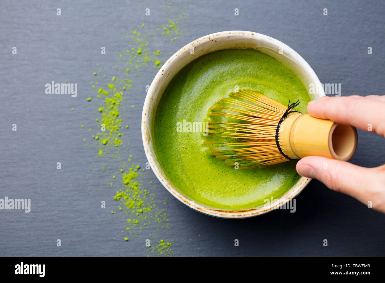 Tè verde Matcha il processo di cottura in una ciotola con una frusta di bambù. Nero ardesia sfondo. Vista dall'alto. Foto Stock