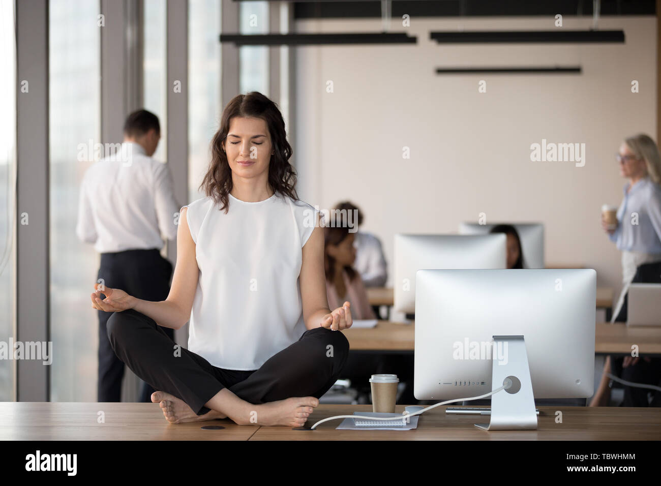Calma impiegato femminile pratica yoga sulla tavola in coworking space Foto Stock