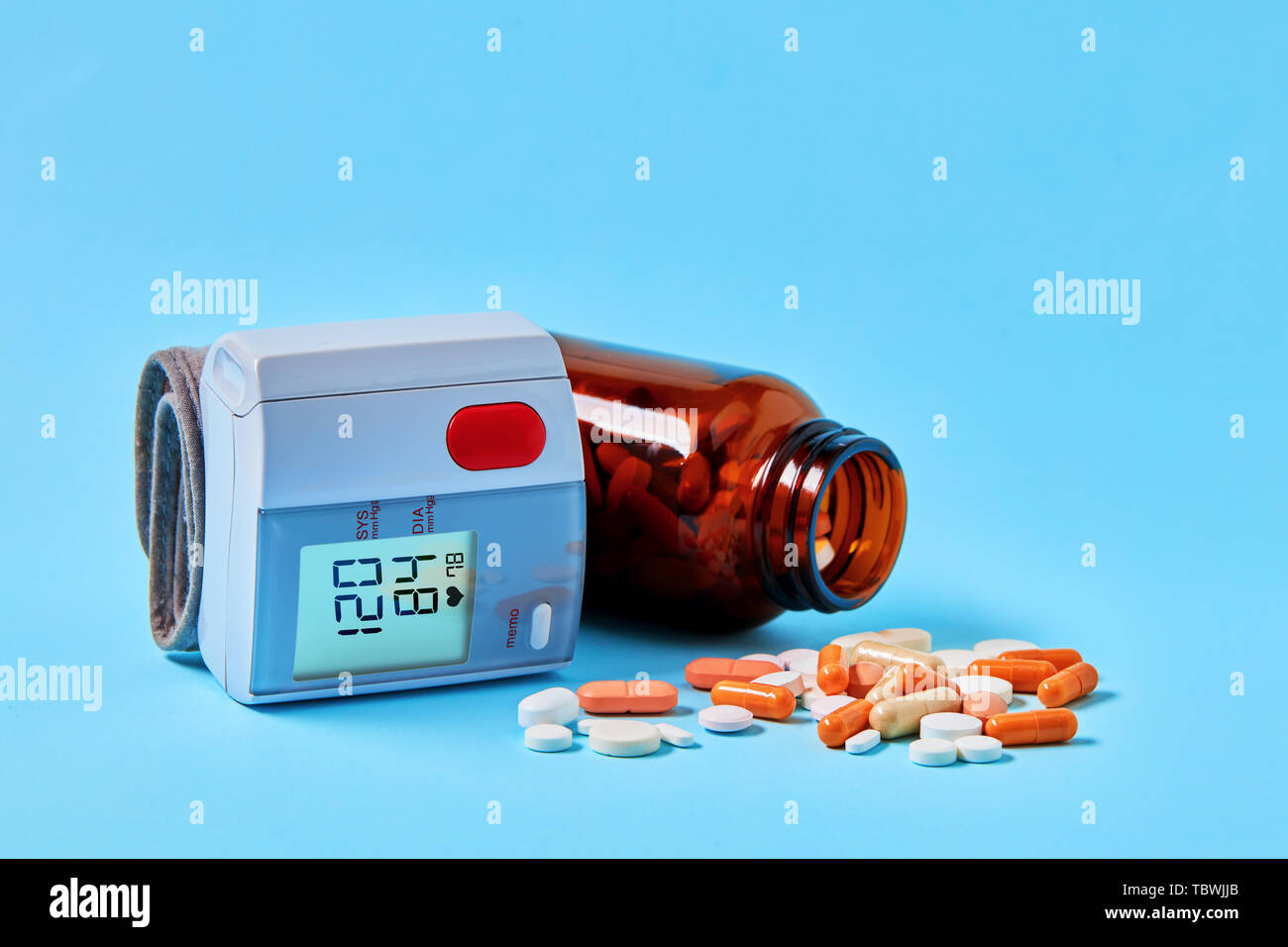 Sangue digitale misuratore di pressione dispositivo di visualizzazione ideale gamma sani e medical pillole versato all'esterno della bottiglia su sfondo blu Foto Stock