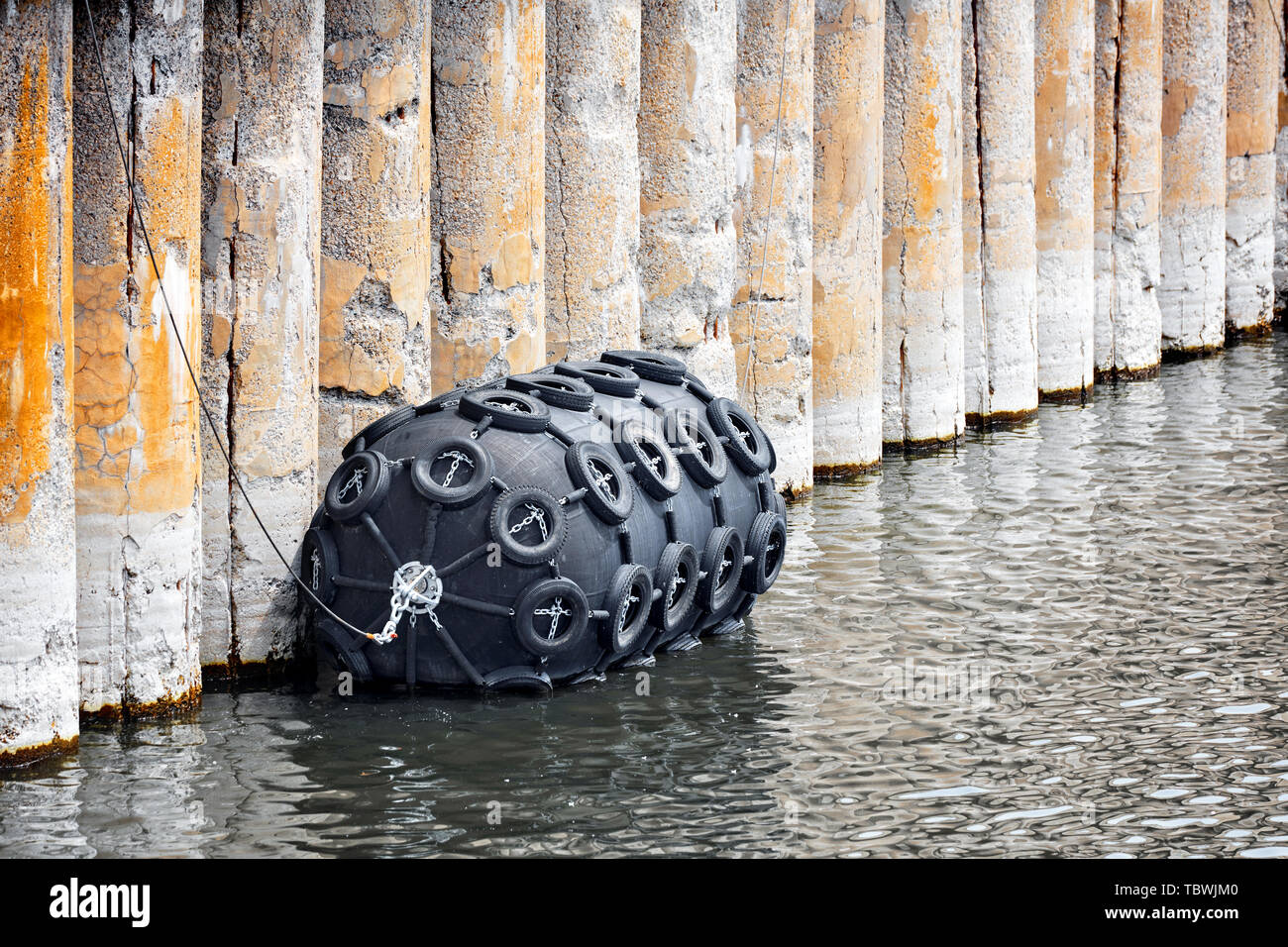 Grande in gomma nera del parafango di boa coperto con pneumatici per auto che galleggia sulle acque del porto Foto Stock