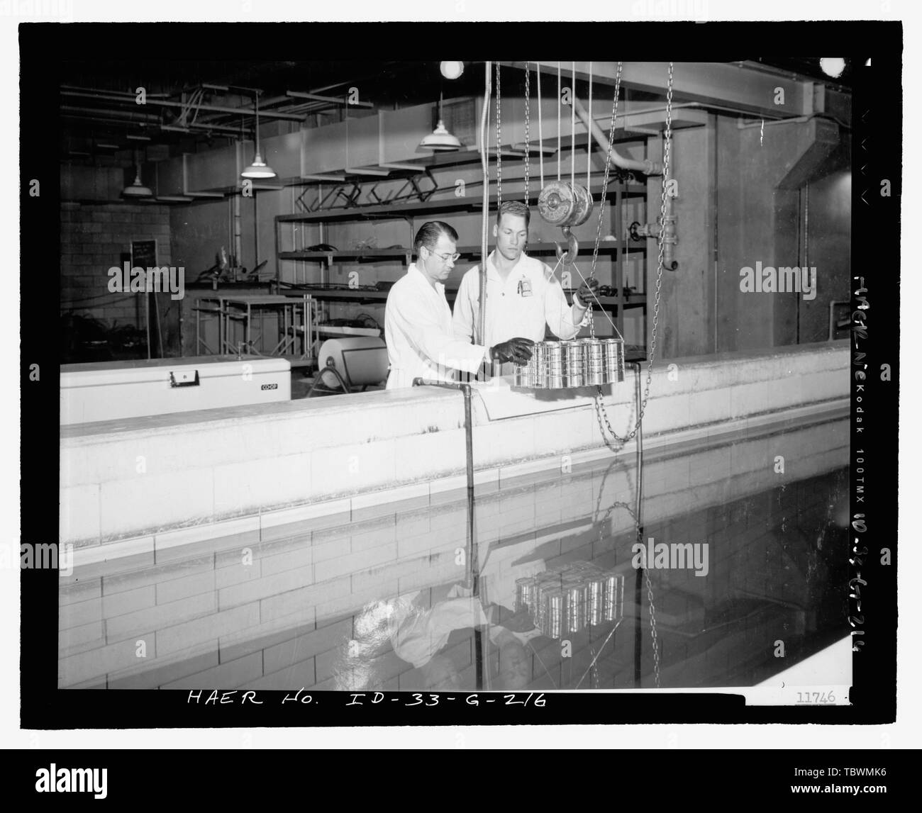 MTR seminterrato. Lavoratori (DON ALVORD E CIRILLO VAN ORDEN della Phillips Petroleum Co.) pongono per irradiazione gamma esperimento nel canale di MTR. Le lattine di cibo sarà abbassato al fondo del canale, dove trascorse MTR, GLI ELEMENTI DI COMBUSTIBILE emettono radiazioni gamma. INL negativo n° 11746. Fotografo sconosciuto, 8201954 Idaho National Engineering Laboratory, Test Area reattore, materiali e test di progettazione di reattori, Scoville, Butte County, ID Foto Stock