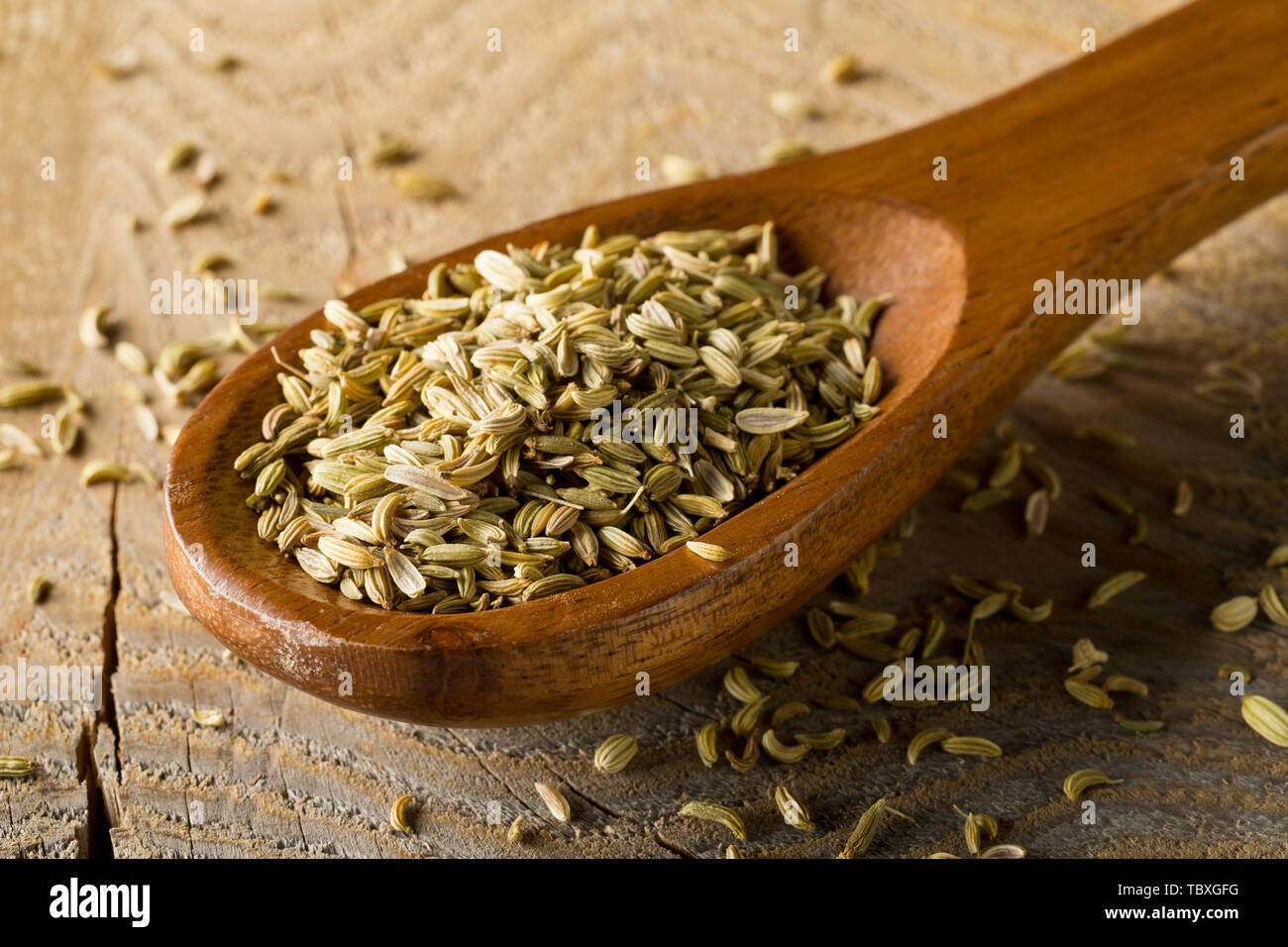 Essiccato semi di finocchio in cucchiaio di legno marrone sul pannello di legno con uno sfondo con messa a fuoco selettiva Foto Stock