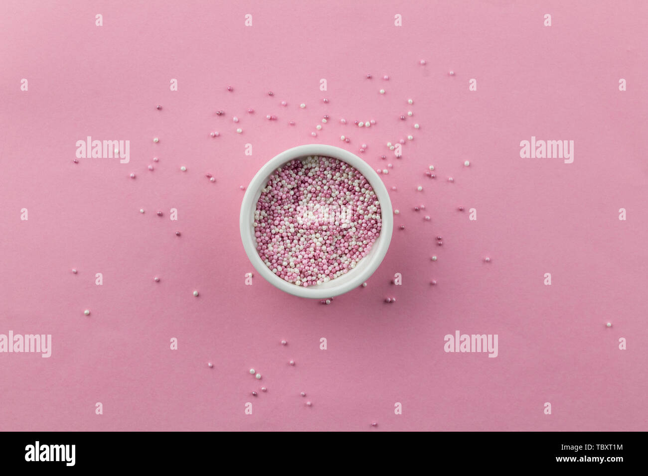 Spruzza isolato su sfondo rosa - little white ciotola con perla torta rosa topping spruzza e sparse su rosa - vista superiore Foto Stock