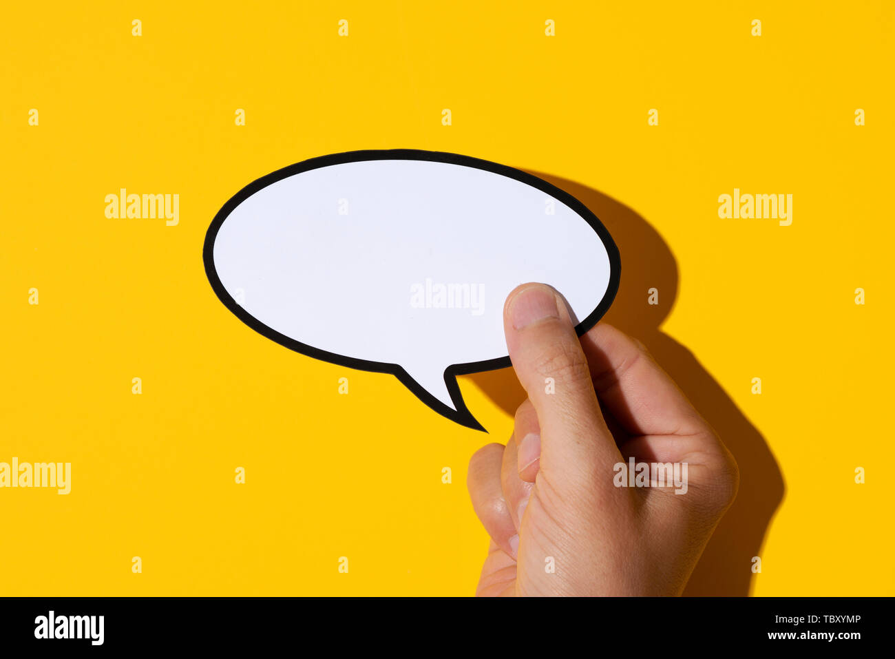 Primo piano della mano di un giovane uomo caucasico tenendo un discorso vuoto palloncino contro uno sfondo giallo, con un disco ombra Foto Stock
