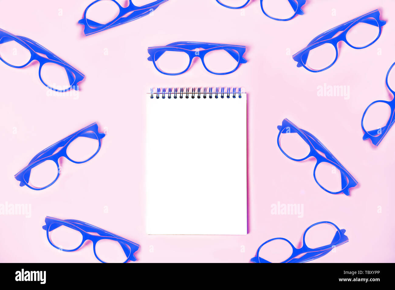 Blocco note con eleganti vetri blu pastello su sfondo rosa. Foto Stock