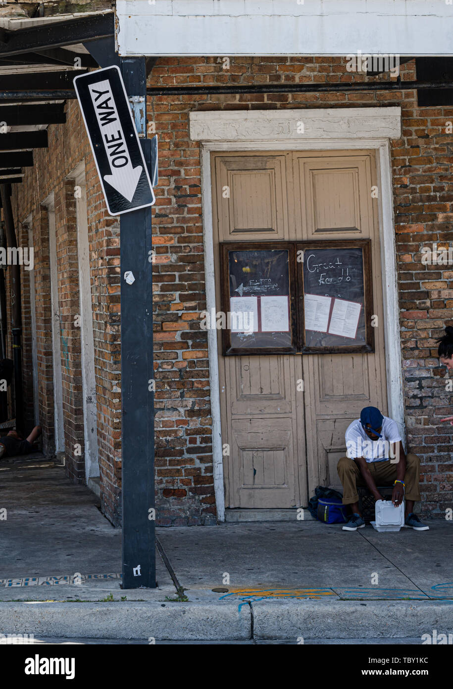 New Orleans, LA, Stati Uniti d'America -- Maggio 23, 2019. Un uomo si siede alla porta di un vecchio Saloon; una rotta in un modo segno punti verso il basso. Foto Stock