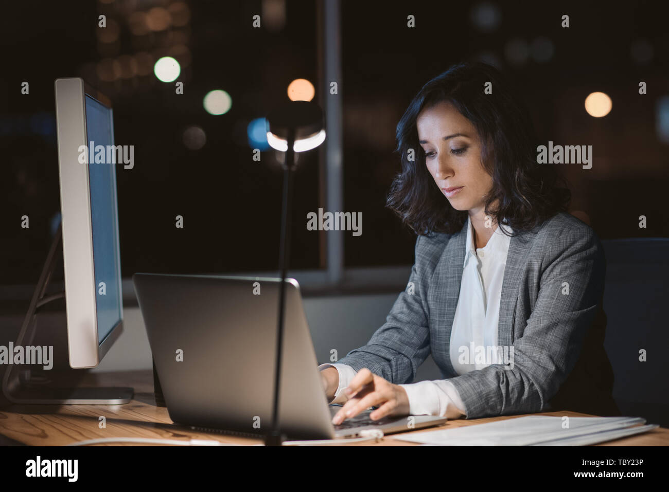 Giovane imprenditrice usando un computer portatile nel suo ufficio di notte Foto Stock