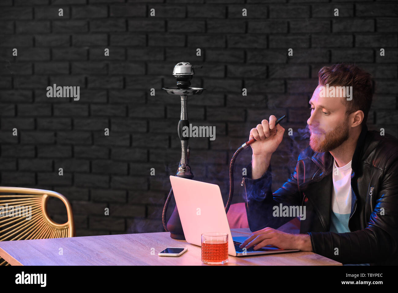 Giovane uomo di fumare narghilè mentre si lavora sul computer portatile in  cafe Foto stock - Alamy