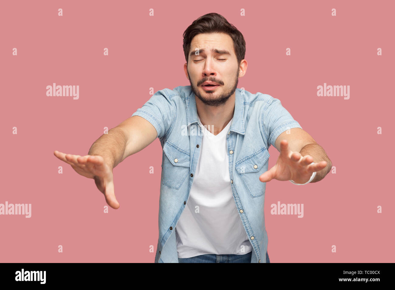 Loneless e la cecità. Ritratto di perso preoccupare barbuto giovane uomo in blu T-shirt casual in piedi con gli occhi chiusi e provare a toccare qualcosa o trovare. Foto Stock