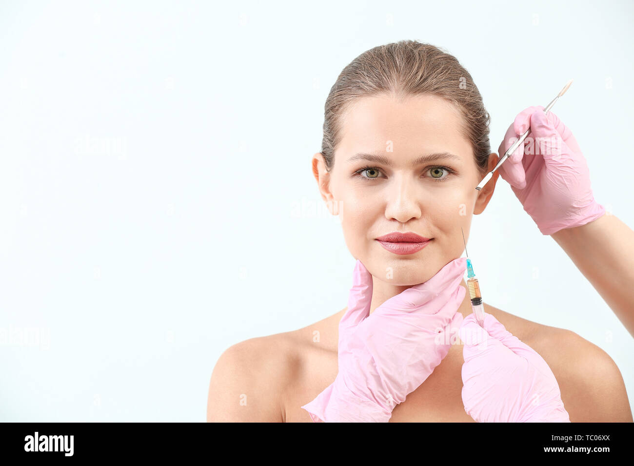 Giovane donna e le mani dei chirurghi plastici su sfondo chiaro Foto Stock