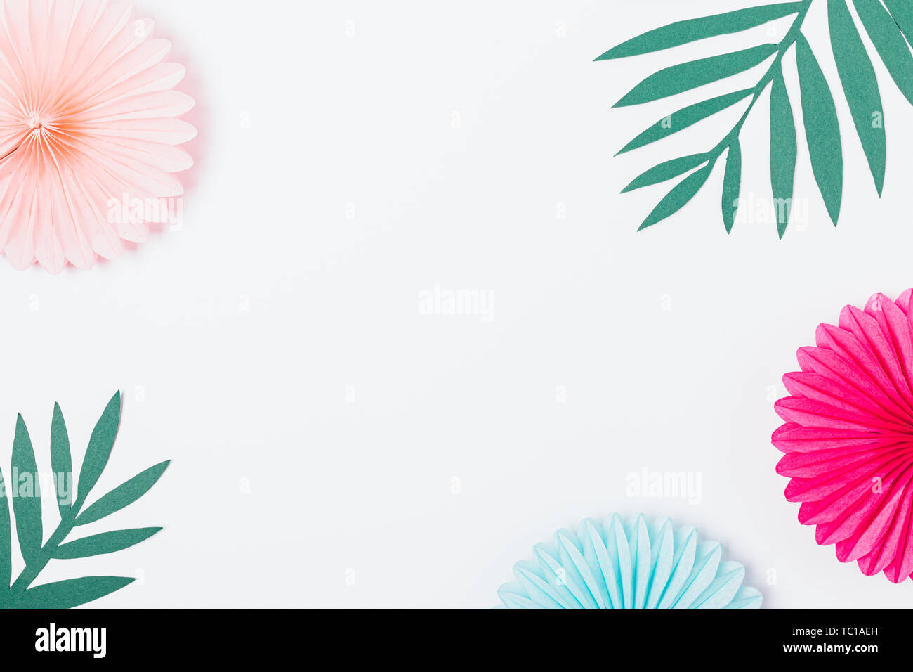 Carta tagliata palm foglie tropicali accanto alla festosa di decorazioni su sfondo bianco con spazio libero nel centro, laici piana. Foto Stock