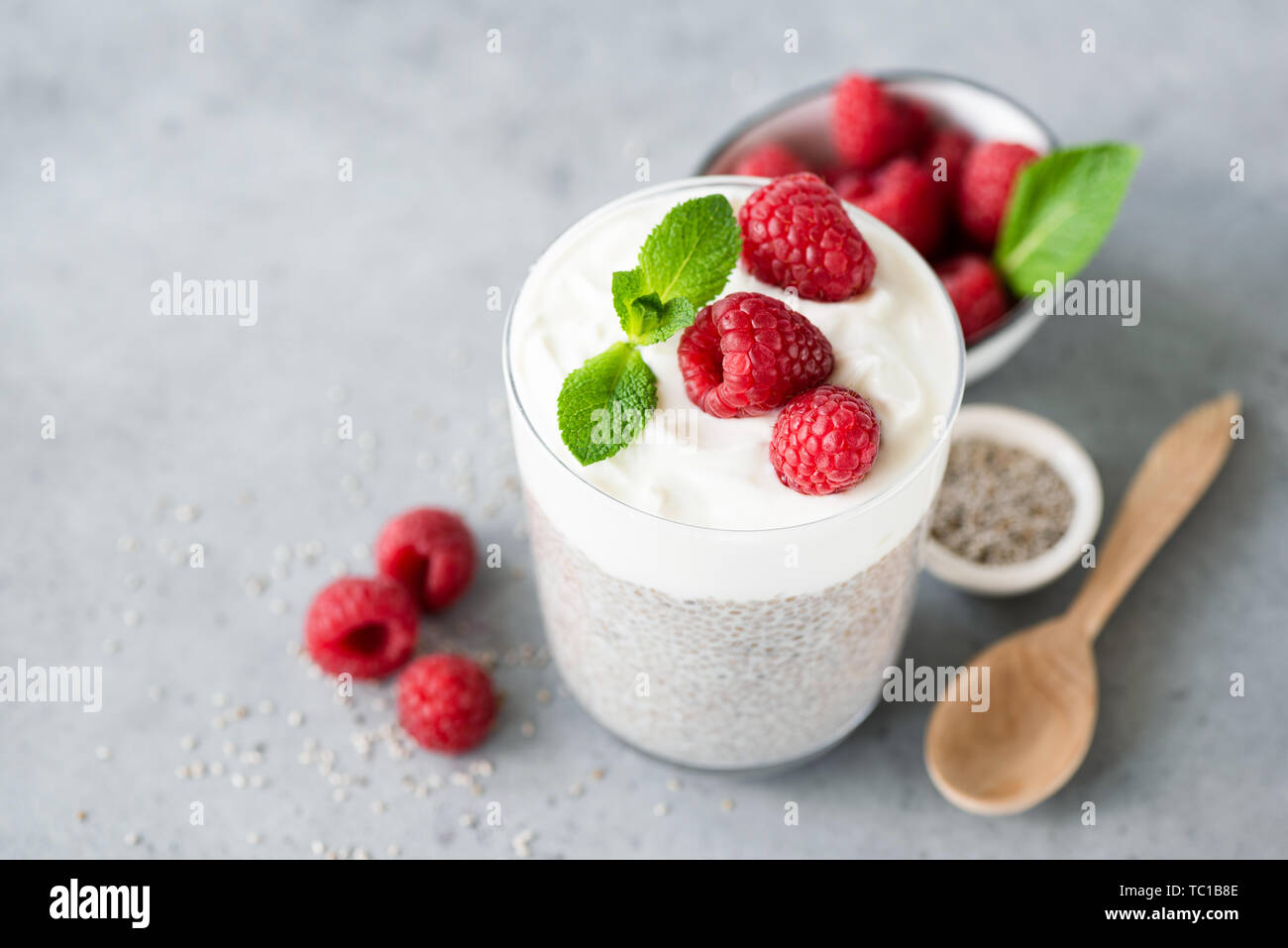 Yogurt Greco budino di Chia con bacche rosse in vetro. Sul cemento grigio sfondo, copia spazio per il testo. Benessere, per la perdita di peso, mangiare sano concetto Foto Stock