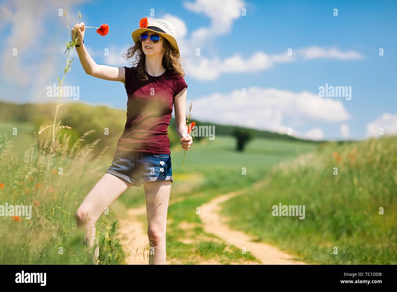 Una giovane ragazza in hat è spiumatura un papavero fiori dal carrello road Foto Stock