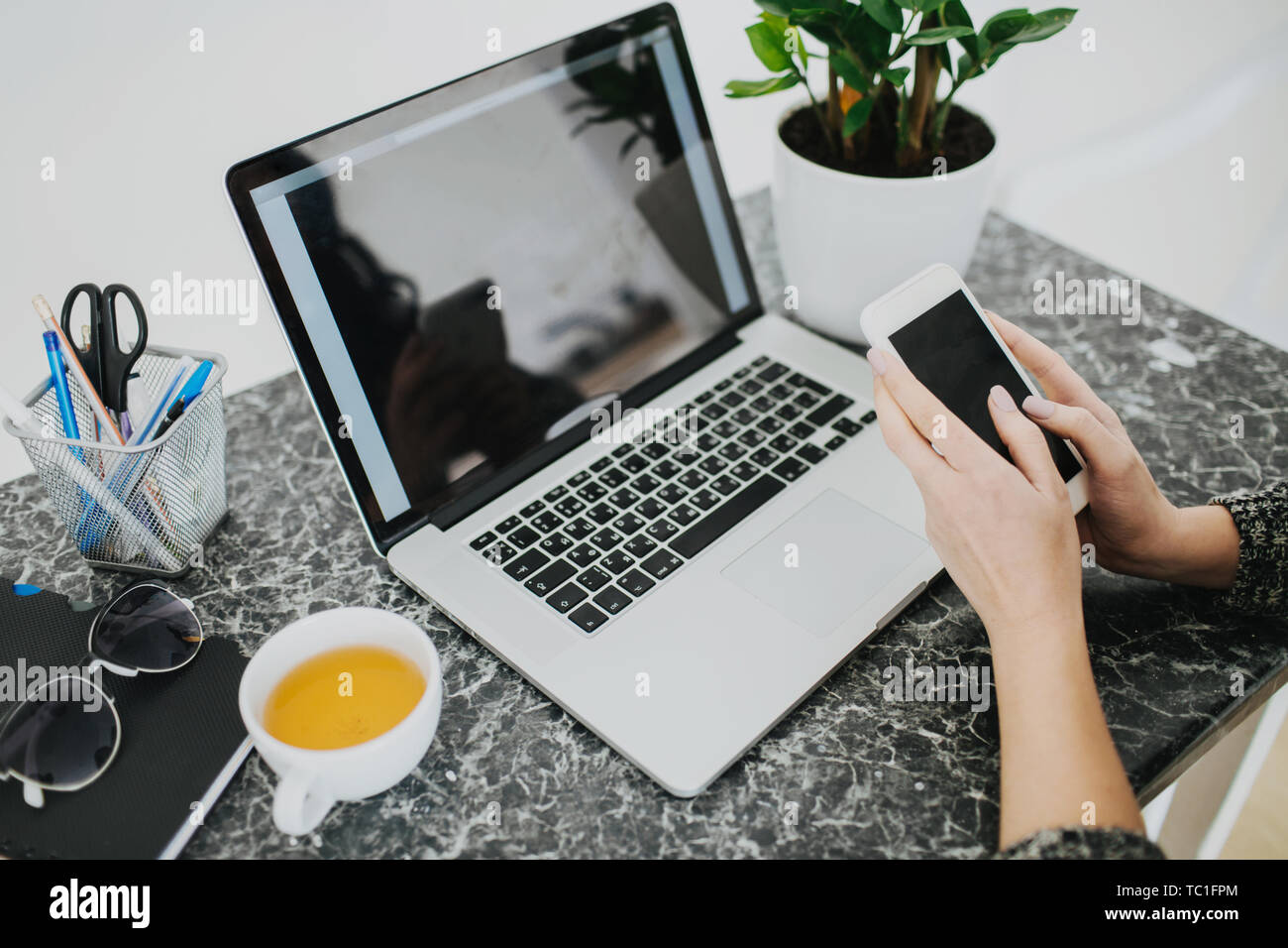 Giovane donna che lavora da casa. Bere tè caldo, tenendo il telefono cellulare e il controllo dei messaggi. Foto Stock