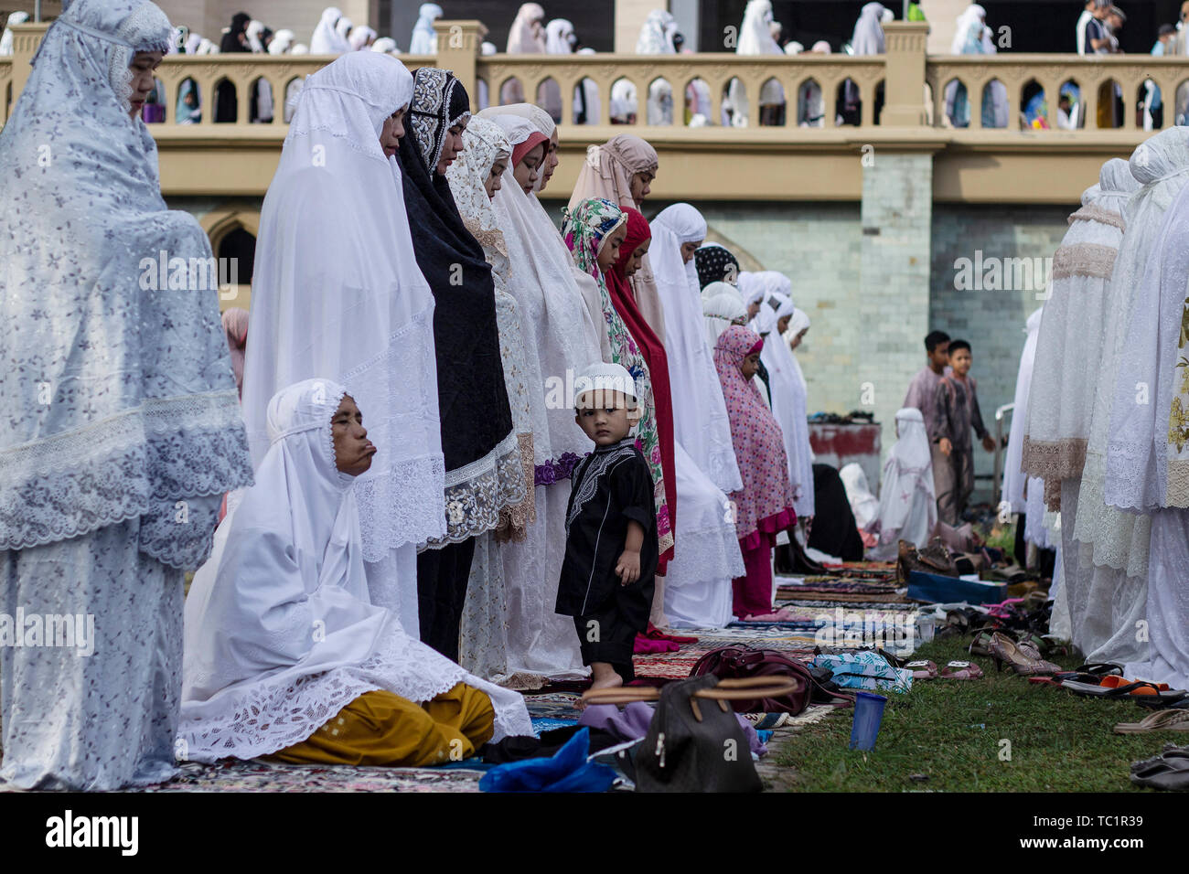Un ragazzo musulmano stand con le donne offrendo preghiere Eid al-Fitr preghiera in Lhokseumawe. I musulmani di tutto il mondo celebrano l'Eid al-Fitr contrassegnato entro la fine del digiuno del mese sacro del Ramadan. Foto Stock