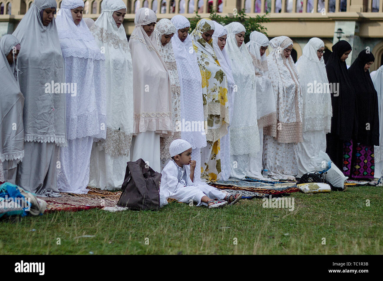Un ragazzo musulmano si siede tra le donne offrendo preghiere Eid al-Fitr preghiera in Lhokseumawe. I musulmani di tutto il mondo celebrano l'Eid al-Fitr contrassegnato entro la fine del digiuno del mese sacro del Ramadan. Foto Stock